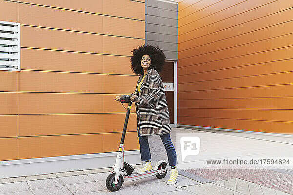 Woman with electric push scooter standing on footpath