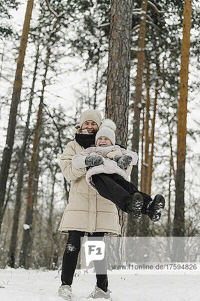 Cheerful mother playing with daughter in winter forest