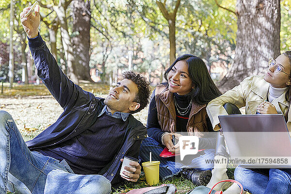 Smiling man taking selfie with friends on smart phone in college park