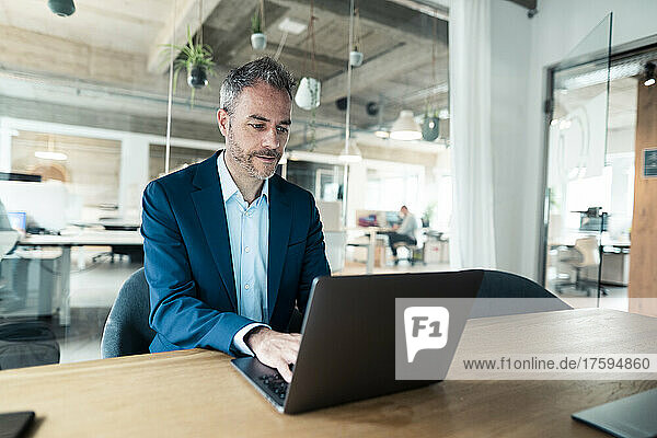 Confident businessman using laptop sitting at desk in office