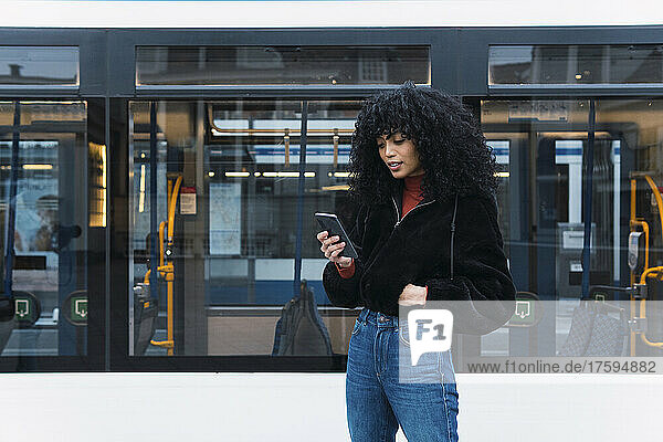 Fashionable young woman using smart phone in front of tram