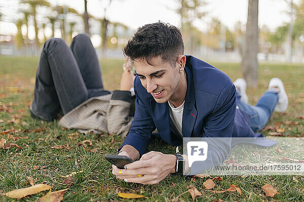 Businessman using smart phone relaxing with colleague in public park