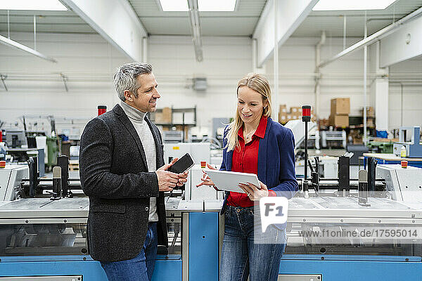 Smiling businessman discussing with colleague using tablet PC by machinery in factory