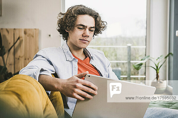 Young man with laptop sitting on sofa in living room at home