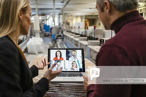 Businesswoman and businessman discussing with colleagues through video call on laptop in factory