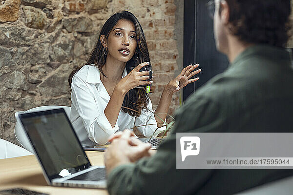 Businesswoman holding coffee mug discussing with businessman at desk in office
