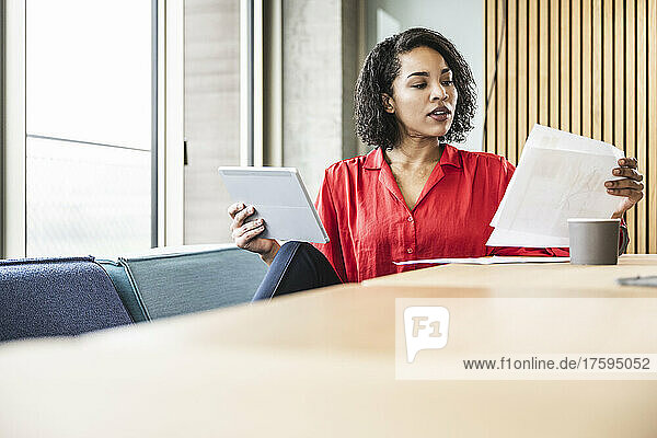 Young businesswoman with tablet PC examining documents in office