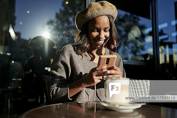 Smiling woman with beret photographing coffee cup on table at cafe