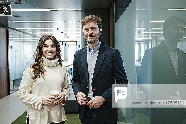Smiling businesswoman with businessman standing by glass wall in office