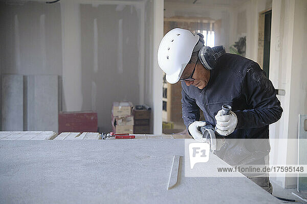 Construction worker cutting sheetrock with power tool at site