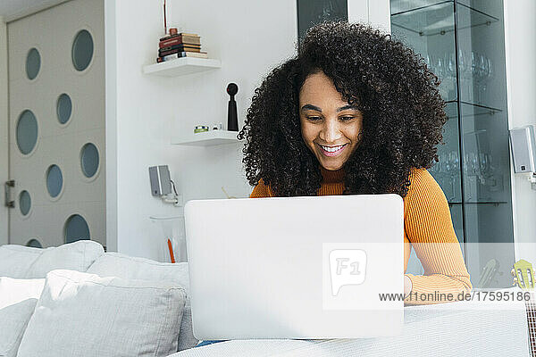 Smiling woman using laptop sitting on sofa at home