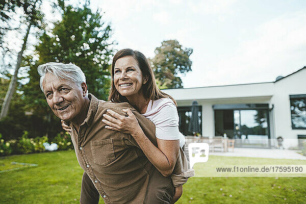 Glückliche Frau genießt die Huckepackfahrt  die ihr ein älterer Mann im Hinterhof gibt