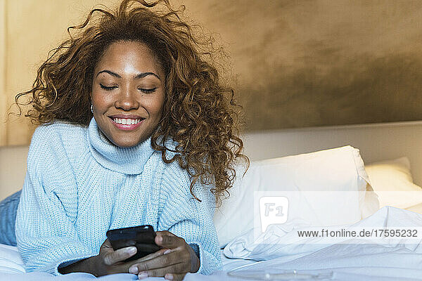 Smiling woman text messaging on smart phone in bedroom