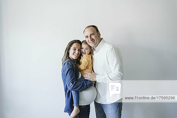Happy parents with cute daughter standing by wall