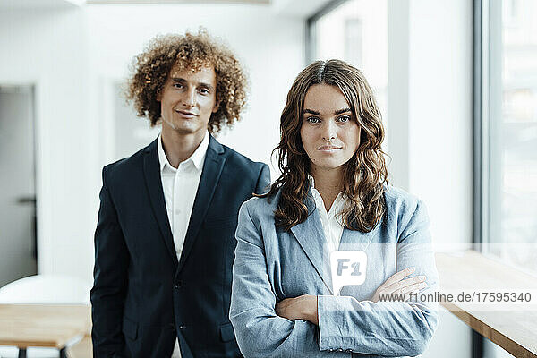 Confident businesswoman with arms crossed standing in front of businessman in office