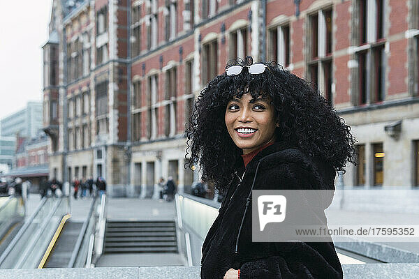 Smiling young curly haired woman looking over shoulder in city