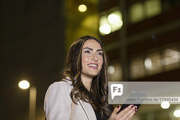 Happy young woman with smart phone at night