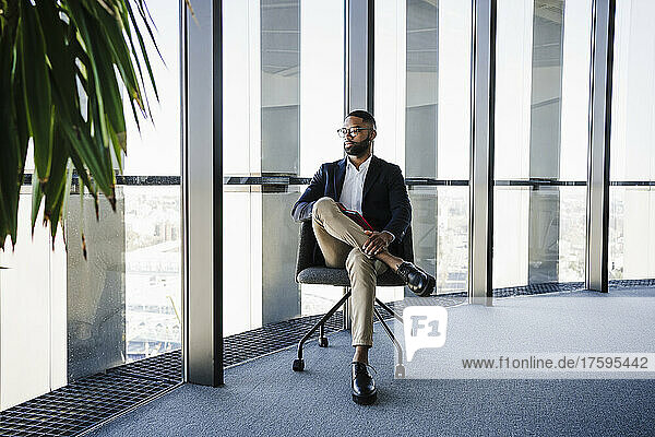 Businessman sitting on chair near glass window in office