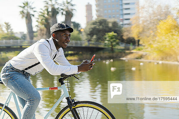 Young man with mobile phone on bicycle day dreaming in city