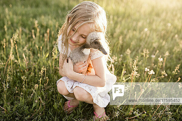 Cute girl embracing baby duck in meadow