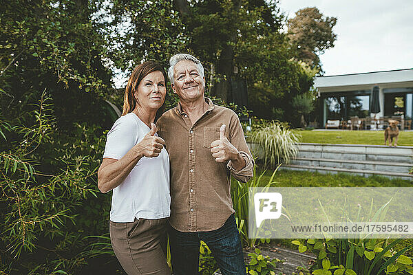 Smiling man and woman gesturing thumbs up at backyard