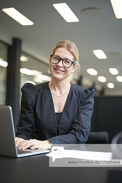 Smiling businesswoman with laptop at office desk