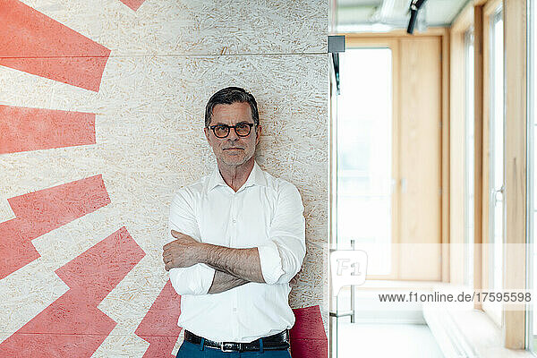 Businessman with arms crossed standing in front of patterned wall at office