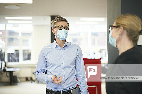 Businessman wearing protective face mask talking with colleague in office