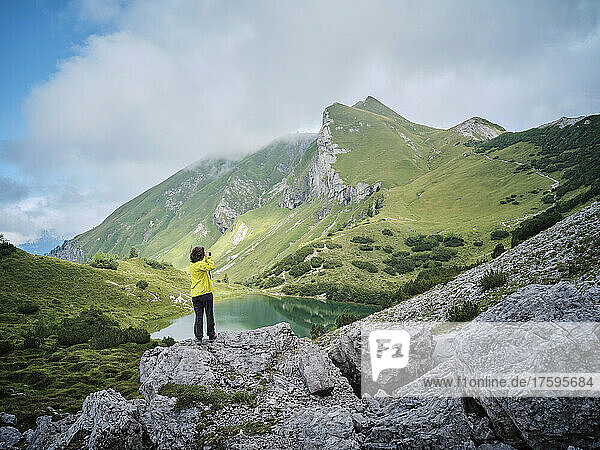 Frau steht auf einem Felsen und fotografiert Berge