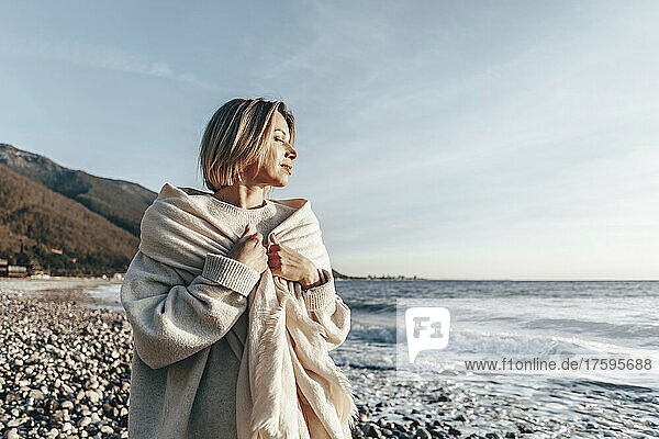Blond woman wrapped in blanket enjoying sunset at beach