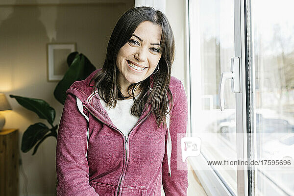 Beautiful happy woman standing by window at home