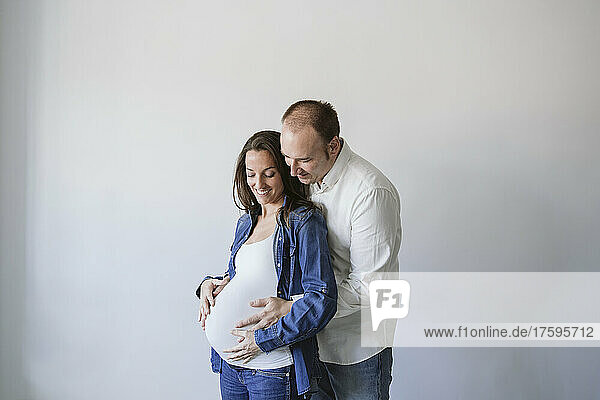 Man hugging happy pregnant woman by wall
