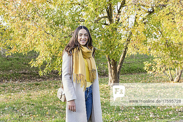 Lächelnde junge Frau mit gelbem Schal steht im Herbstpark