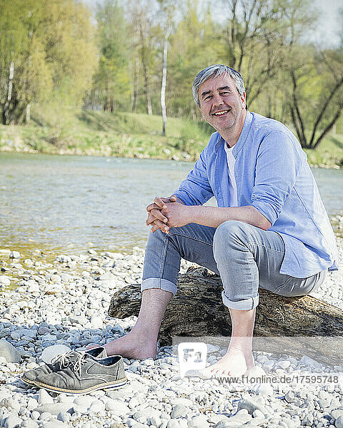 Smiling man sitting on driftwood by river
