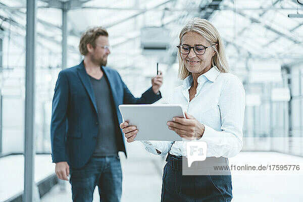 Smiling businesswoman using tablet PC with colleague in background at office