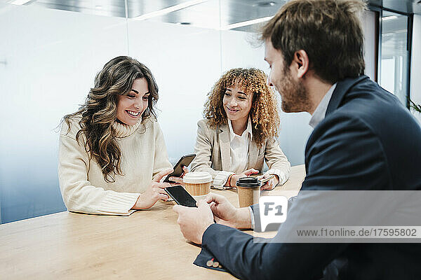 Smiling businesswomen and businessman with smart phones enjoying coffee break