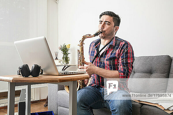 Musician teaching saxophone on video call through laptop at home