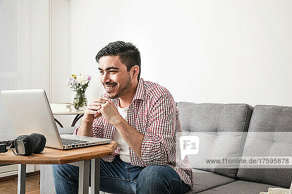 Happy freelancer with hands clasped attending video call through laptop at home