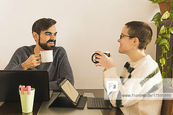 Happy colleagues drinking coffee at desk in small office