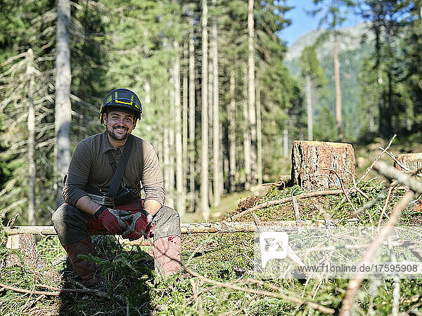 Smiling logger sitting on fallen tree in forest