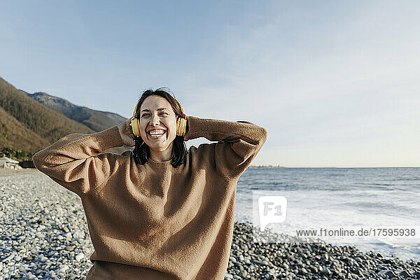 Cheerful young woman enjoying music through headphones at beach