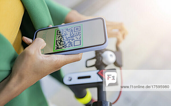 Commuter scanning QR code through smart phone on electric push scooter