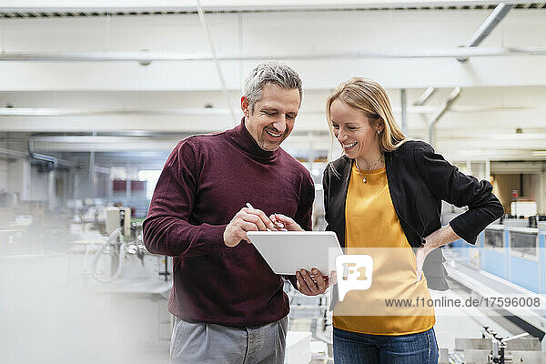 Happy businesswoman and businessman sharing tablet PC in industry