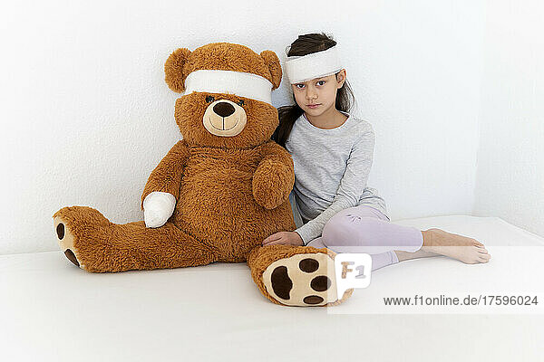 Bandage on girl with teddy bear sitting in front of white wall
