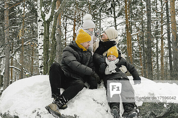Man and woman sitting with daughter and son on snow in winter forest