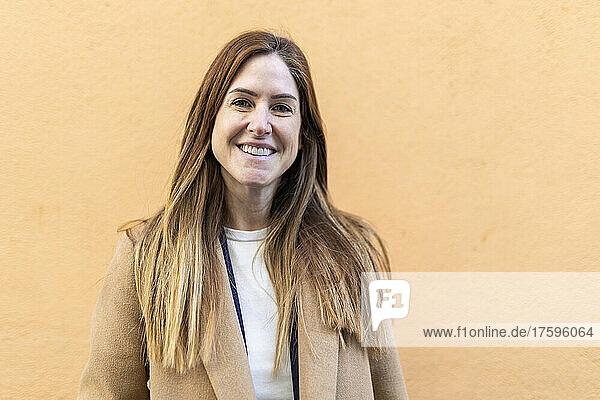 Lächelnde Frau mit braunen Haaren vor der Wand