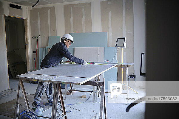Construction worker measuring sheetrock on workbench at site