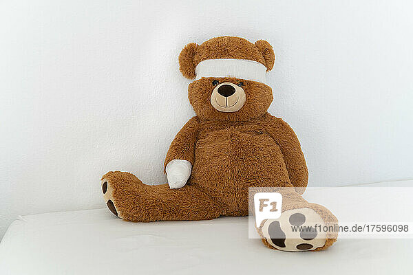 Brown teddy bear with bandage on bed