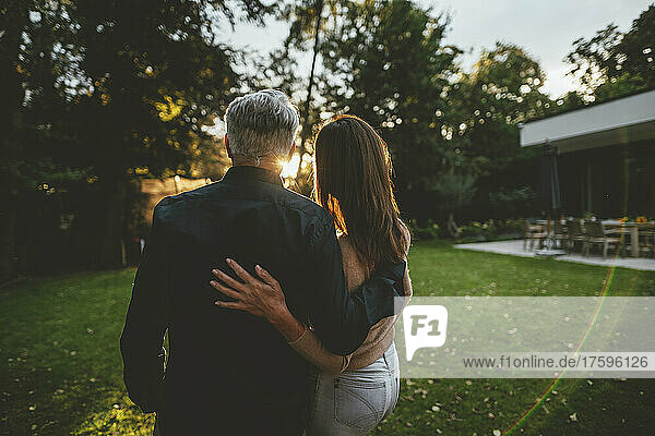 Couple standing with arms around in garden at sunset