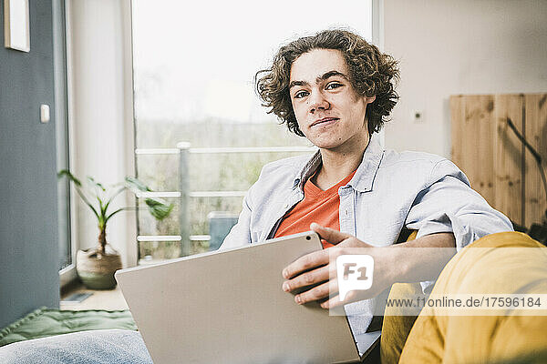 Smiling man with laptop sitting on sofa in living room